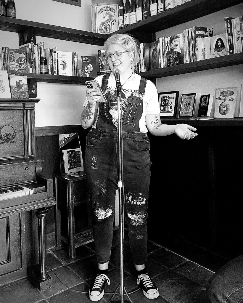 Lauren Parker reads in Golden Sardine in front of a microphone, surrounded by books. 